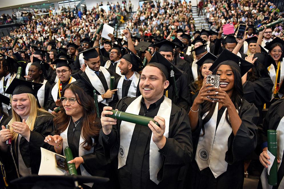 GGC grads standing during ceremony with audience in background