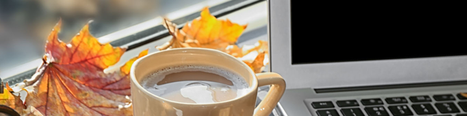 laptop next to fall leaves and cup of cocoa