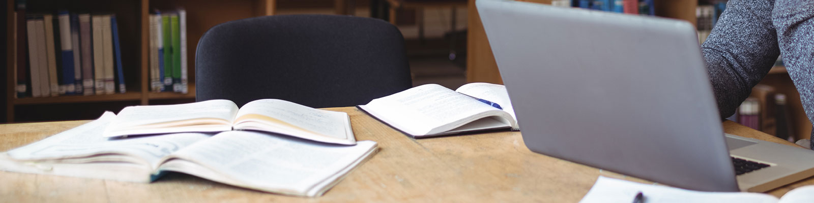 student studying in library with laptop and open books