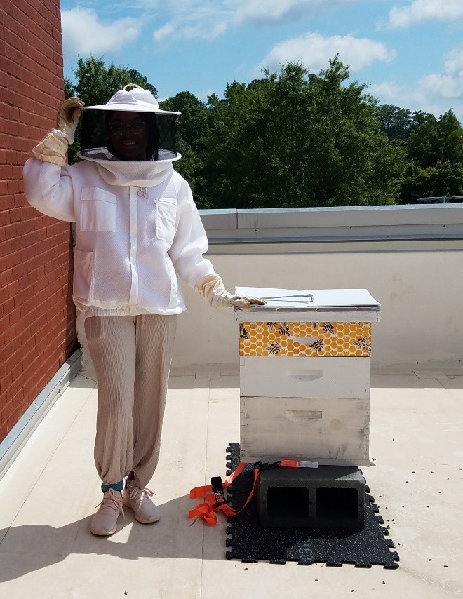 Giana Jeanty, a Chemistry major, installs a hand-painted honey super of her own design, blending science and creativity to support campus beekeeping efforts.
