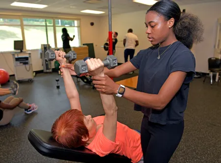 Exercise science student helping a a woman life weights