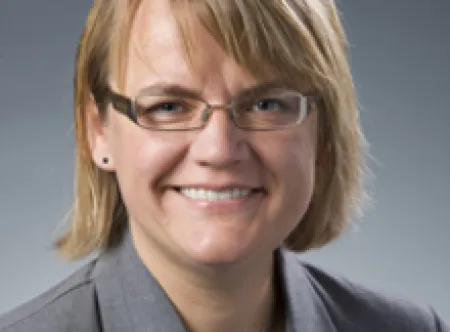 Dr. Dovile Budryte wearing glasses and gray jacket smiling at camera