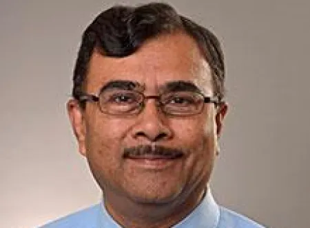 Dr. Atul Saxena wearing a blue dress shirt and tie, wearing glasses and smiling at camera
