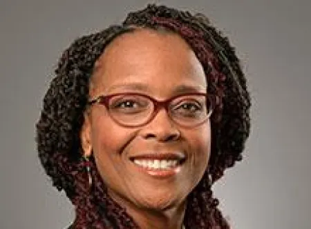 Dr. Alvina Atkinson wearing a black jacket, red shirt, brown-rimmed glasses and black smiling at the camera