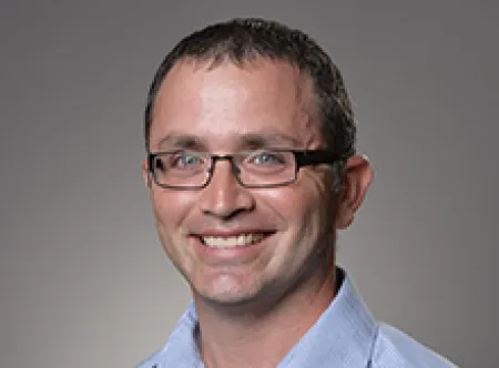 Dr. Peter Sakaris wearing a light blue shirt and glasses smiling at camera
