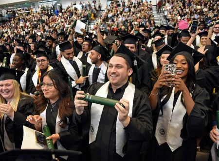 GGC grads standing during ceremony with audience in background