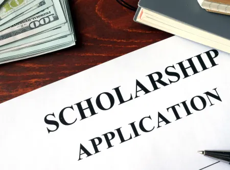 White paper with scholarship application written at the top, a stack of money and two notebooks