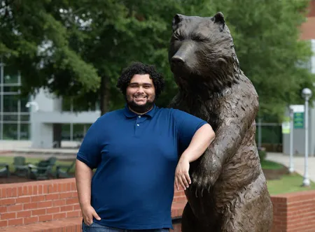 Antavius Cain, 2020 biology grad, posing with the Grizzly statue
