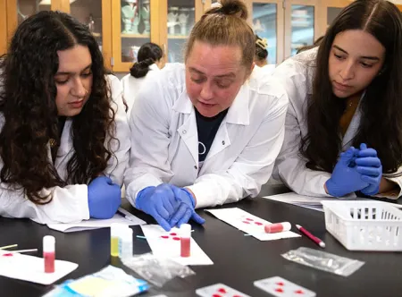 Dr. Victoria Bali, middle, shows Mehak Moti (left) and Noor Daoud (right) how to see the clotting in a blood sample and determine the blood type