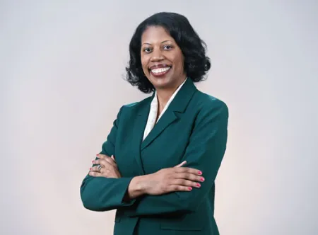 Dr. Chavonda Mills posing for camera and wearing green jacket and white shirt with arms folded