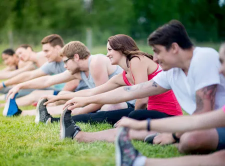 Students stretching while seated on the grass