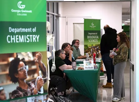 Event participants stop at the Biological Sciences table to ask professors questions about the major