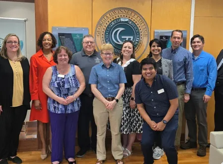 A group of 12 faculty members posing for a picture with the college president in an office