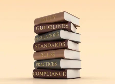 Getty Images stack of seven books on a table with a word written on the binder of each, including Policy, Guidelines, Regulations, Standards, Rules, Practices and Compliance