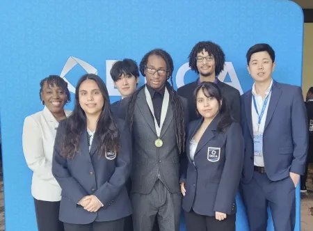 Five students and two faculty advisors pose in front of a sign that says DECA.