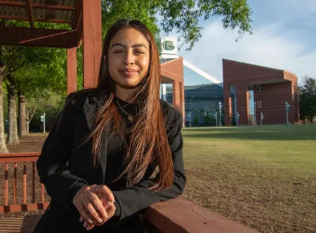 A student smiling with a campus building in the background.