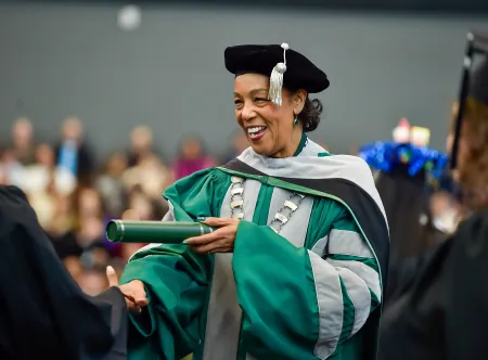 President Jann L. Joseph dressed in commencement cap and gown handing a diploma tube to a graduate during the fall 2025 commencement ceremony