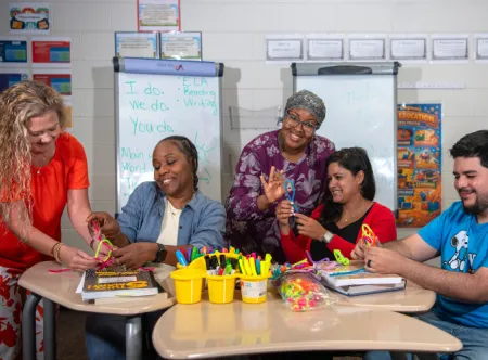 April Ferraro, Nimat Muhammad, Fatoumata Bah, Michelle Saldanha and Will Reyes laugh together as they work on crafts in a classroom.