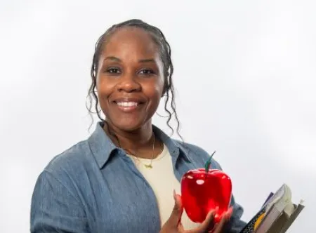 A female teacher holding a red apple in her hand and books in the other hand.