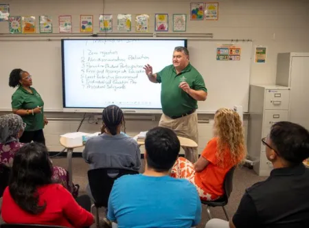 A female and male professor teaching in a classroom with college students.