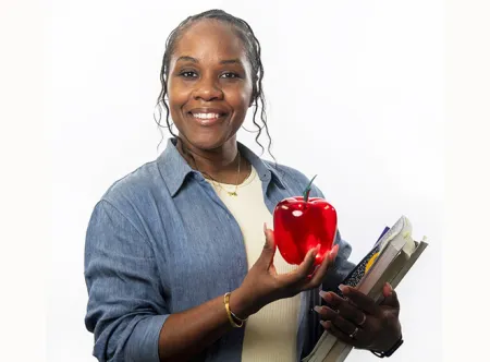 A female teacher holding a red apple in her hand and books in the other hand.