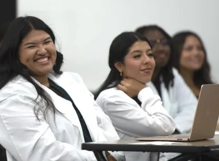Female nursing students smiling during orientation in a classroom.