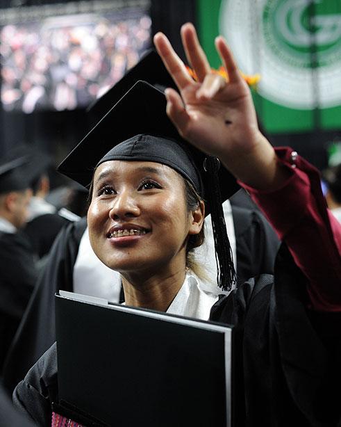 waving female graduate with diploma at commencement