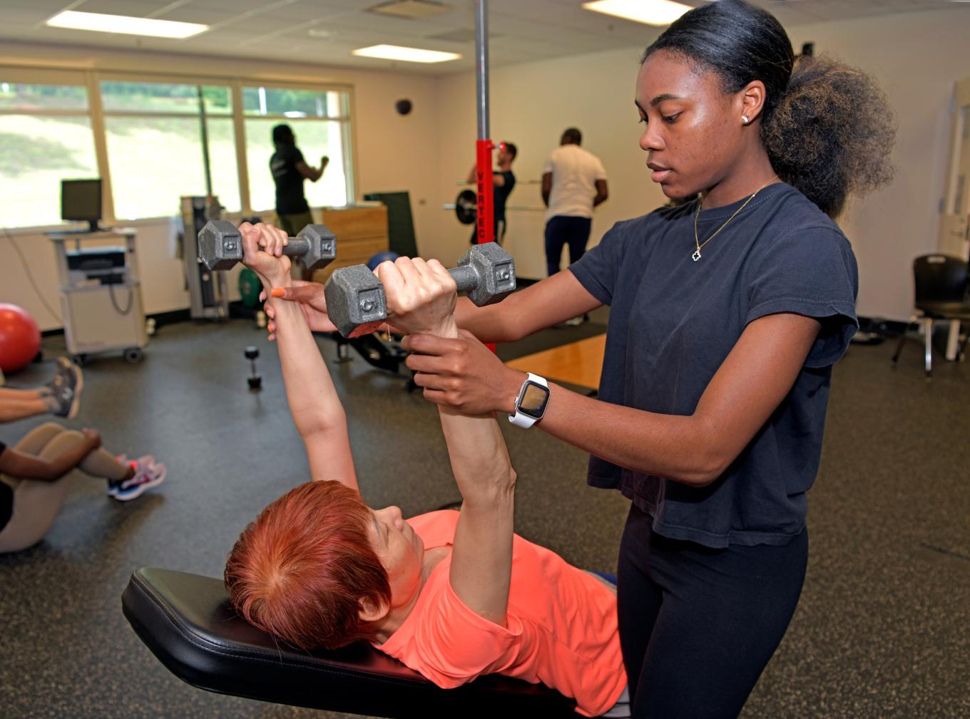 Exercise science student helping a a woman life weights