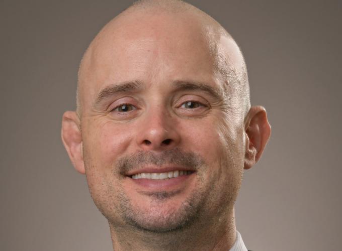 Dr. Matthew Robison wearing a black jacket, white shirt and green bowtie smiling at the camera
