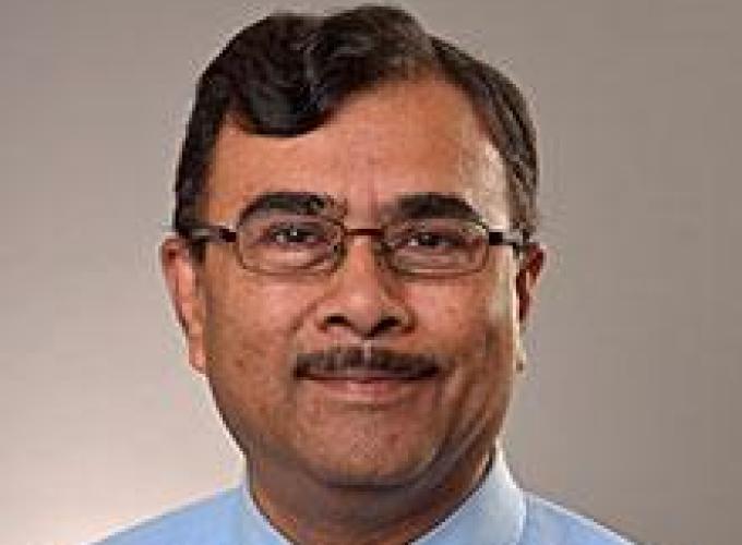 Dr. Atul Saxena wearing a blue dress shirt and tie, wearing glasses and smiling at camera