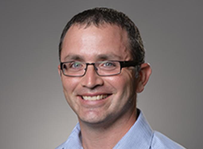 Dr. Peter Sakaris wearing a light blue shirt and glasses smiling at camera