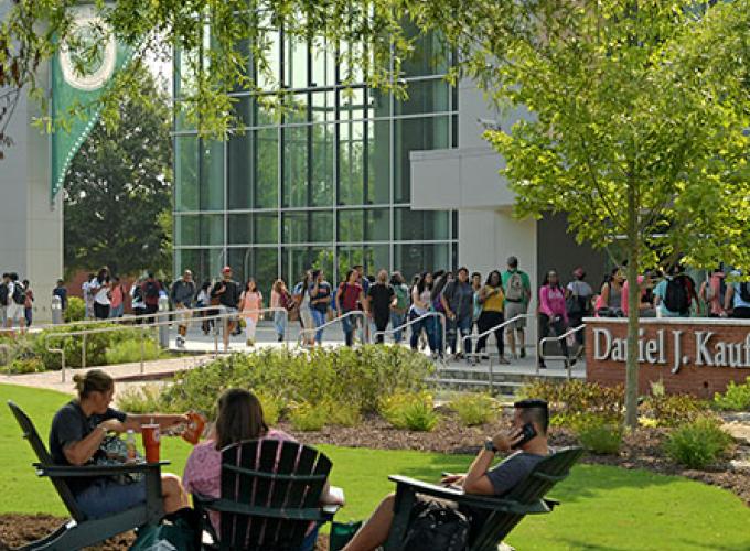 Students in Adirondack chairs with students walking between classes in the background
