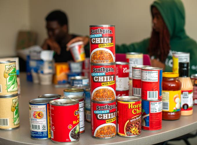 cans of food placed on table in GGC Care Pantry with two staff members in the background