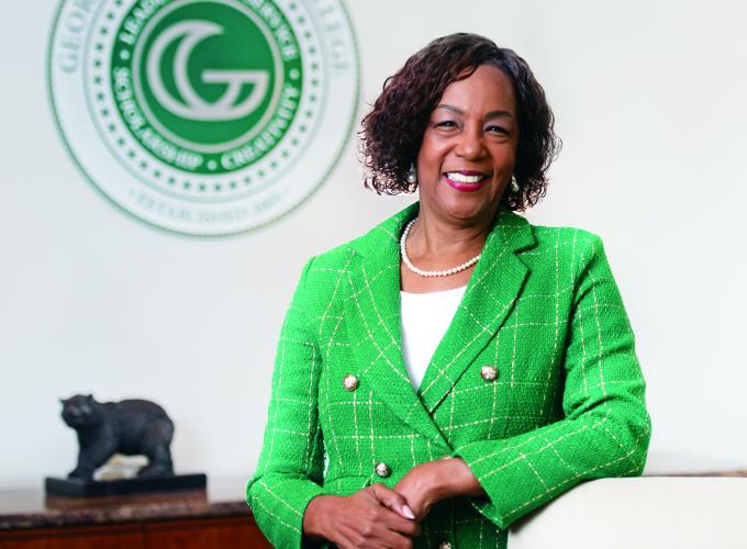 Dr. Jann L. Joseph standing and leaning on a chair for a photo; the GGC college seal shows on a back wall and small Grizzly statue on a desk