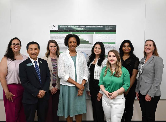 Dr. Jann L. Joseph and Dean Tyler Yu with faculty and staff standing in front of a poster at CREATES 2025