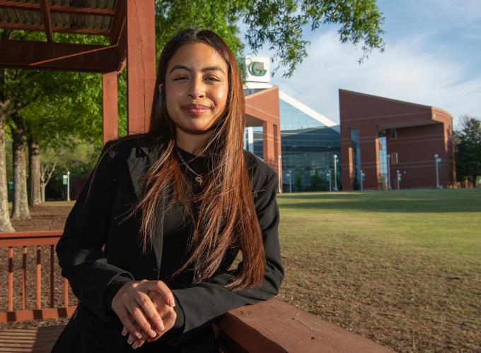 A student smiling with a campus building in the background.