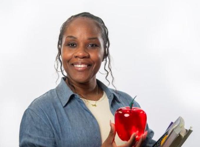A female teacher holding a red apple in her hand and books in the other hand.