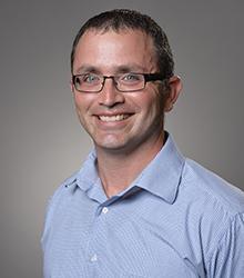 Dr. Peter Sakaris wearing a light blue shirt and glasses smiling at camera