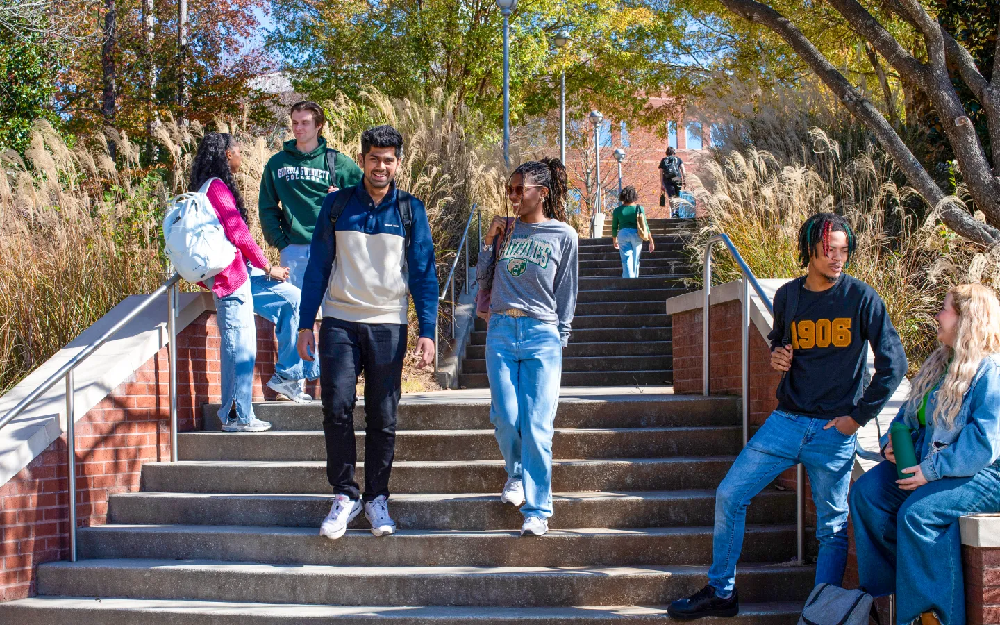 Two students walk down stairs outdoors on GGC's campus. Other students in the foreground and background are chatting with each other. 