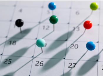 Calendar with colorful push pins scattered on dates 