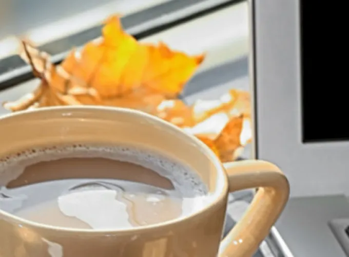 laptop next to fall leaves and cup of cocoa