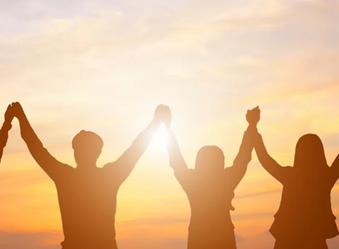 row of students holding up raised hands against sunrise