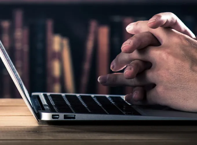 open laptop on table in front of shelves of books