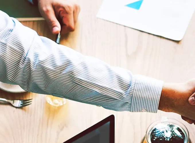 two people shaking hands across table with computer keyboard