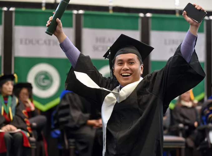 GGC grad on stage with hands raised in celebration