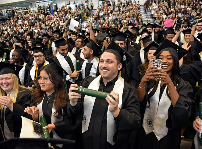 GGC grads standing during ceremony with audience in background
