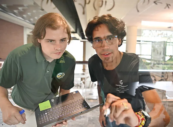 Two students tutoring at the dry erase window in the Academic Enhancement Center