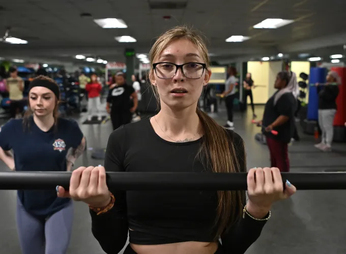 Student curling a weighted bar in exercise class
