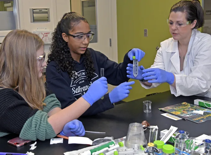 A professor helps two middle school students with a beaker
