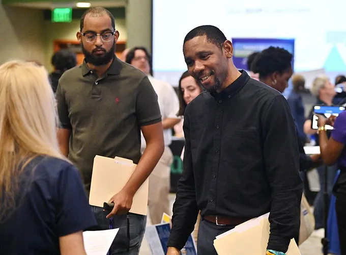 GGC students carrying folders and talking with employer at career fair
